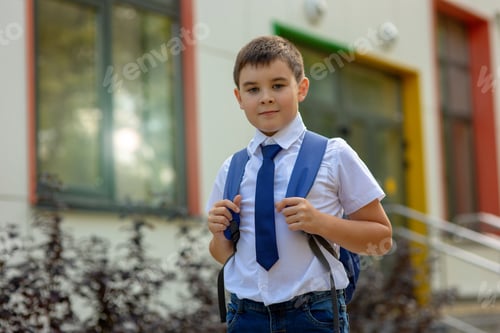 Preview: stylish and young schoolboy in a white shirt and jeans with a backpack in the background of the