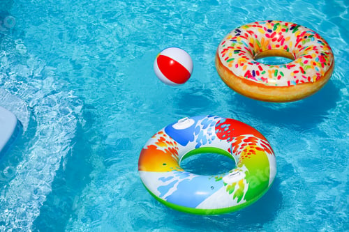 Preview: Bright inflatable rings and beach ball floating in swimming pool on sunny day. Space for text