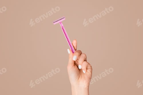 Preview: Young girl showing disposable razor on pink background, closeup of hand