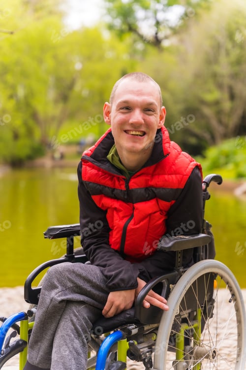 Preview: Portrait of a paralyzed young man in a public park in the city. Sitting in the wheelchair smiling