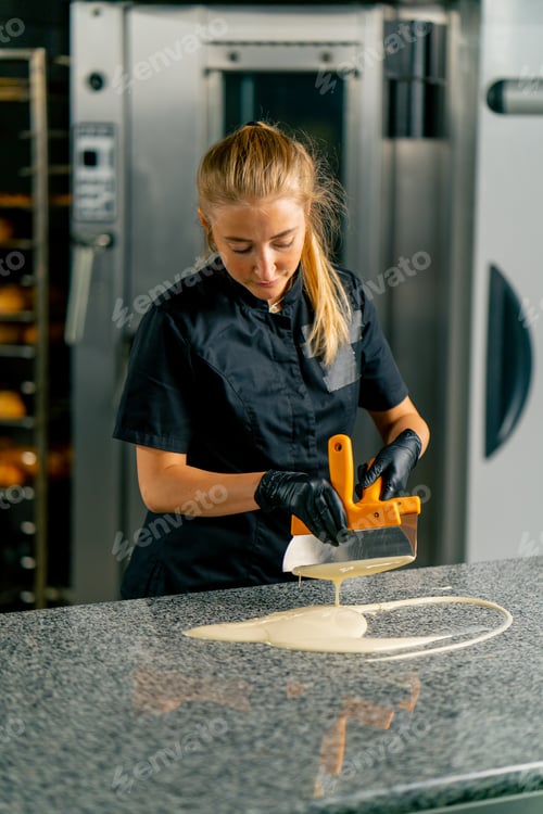 Preview: A young girl pastry chef pours melted hot white chocolate onto the kitchen table to make chocolates
