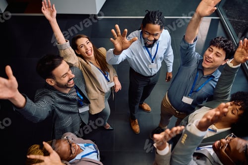 Preview: Multiracial group of business colleagues raising their hands while celebrating success in office.