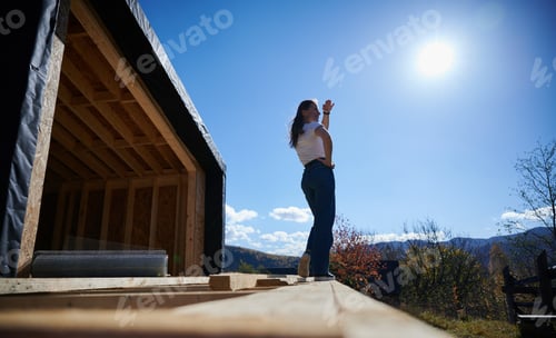 Preview: Woman on terrace at unfinished wooden frame house.