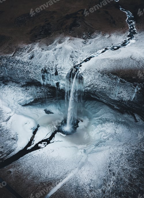 Preview: Vertical shot of a waterfall and a frozen river flowing over the mountains in Iceland