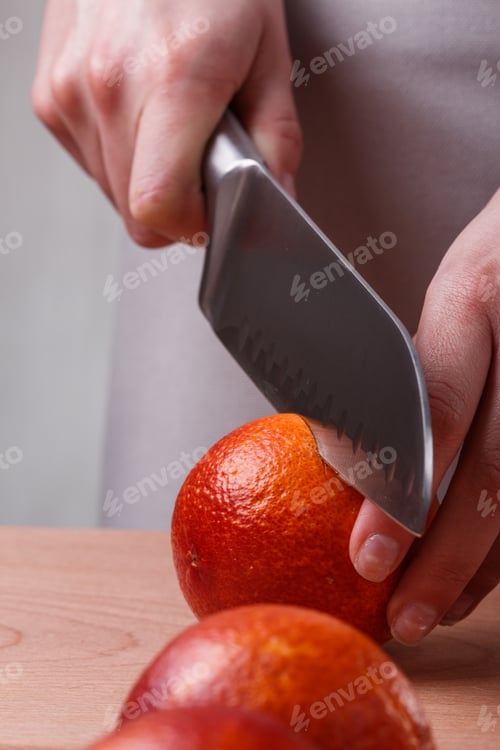 Preview: young woman in a gray apron cuts blood orange