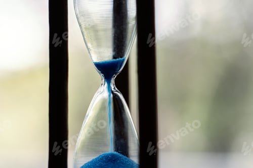 Preview: macro view of a blue sand pouring in the vintage old hourglass