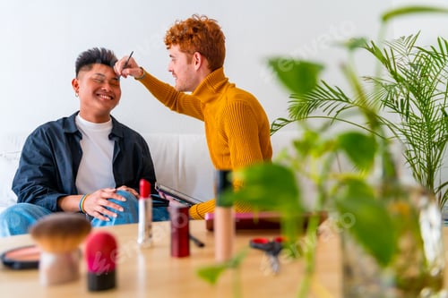 Preview: Beautiful gay couple putting on makeup and having fun being romantic on the sofa, lgbt concept
