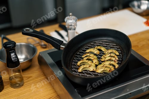 Preview: Professional kitchen chef cooks fresh green avocado in frying pan for frying vegetables