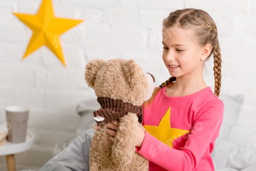 Preview: Blissful kid with braids looking at teddy bear with smile