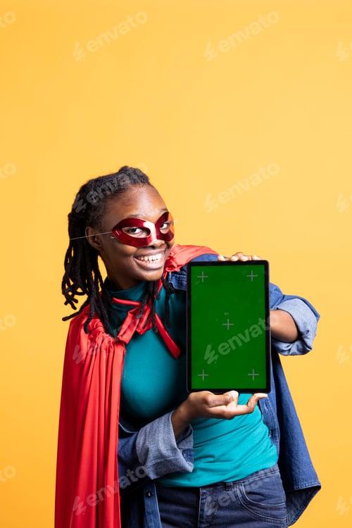 Preview: Girl wearing superhero costume and mask for Halloween holding mockup tablet