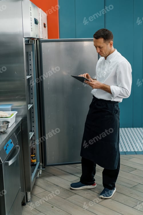 Preview: Professional chef using tablet computer for recipes while working in modern kitchen cooking concept