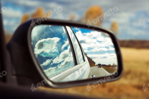 Preview: blue sky with fluffy clouds and road reflection an car mirror on a background of autumn field