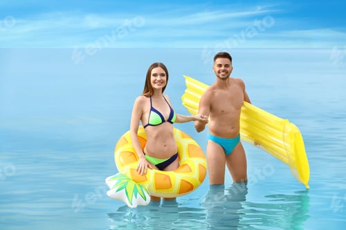 Preview: Young woman in bikini and her boyfriend with inflatable toys on beach. Lovely couple