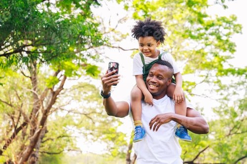 Preview: Happy African American father and son selfie together in the park in the daytime in summer