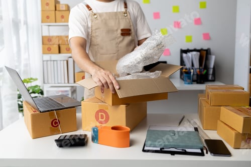 Preview: Male owner of an online store packs products into parcel boxes based on orders from online sales sit
