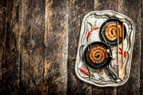 Preview: Sausages in pans on a steel tray with hot chili peppers.