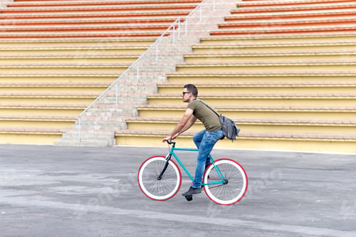Preview: Side view of young man is wearing sunglasses and carrying shoulder bag while riding fixie bike.