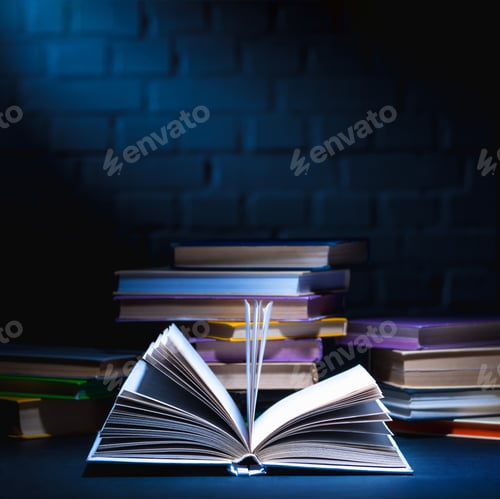 Preview: open book in front of stack of colored books on dark surface