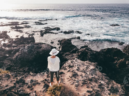 Preview: Above view from the drone that is flying. Elderly woman on a rocky beach at sunset enjoying freedom