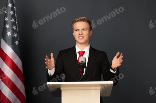 Preview: emotional man gesturing on tribune with american flag on black background