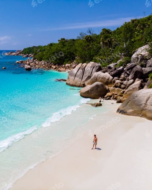 Preview: young man on a white beach with turquoise colored ocean, Anse Lazio beach Praslin Island Seychelles