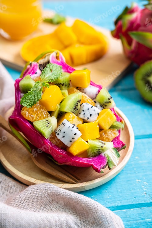 Preview: Mix tropical fruits salad served in half a dragon fruit on wooden table
