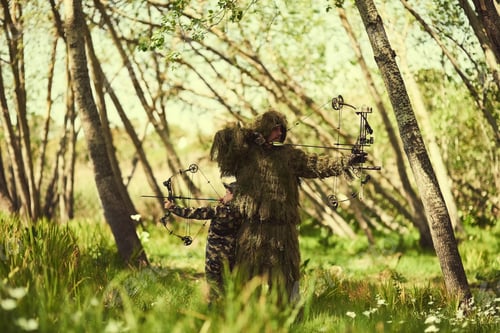 Preview: Shot of a father and son in camouflage hunting with bows and arrows in the woods