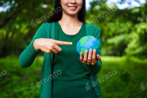 Preview: An Asian woman holds a globe in green forest,symbolizing importance preserving nature.emphasizes