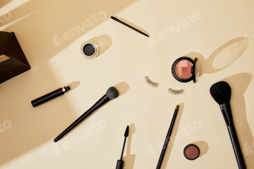 Preview: top view of various cosmetics and false eyelashes lying on beige tabletop