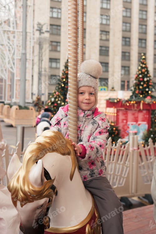 Preview: A joyful girl rides on a Christmas carousel in the square, in the city.