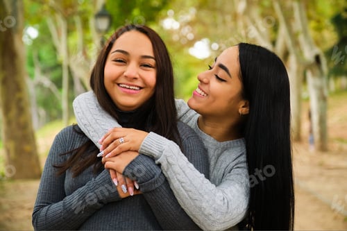 Preview: Happy Latin lesbian couple hugging and smiling in a park.