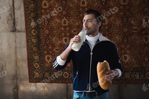 Preview: young man in vintage clothes with bottle of milk and loaf of bread in front of rug hanging on wall