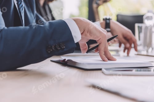 Preview: cropped view of businessman holding pen near notebook at business meeting