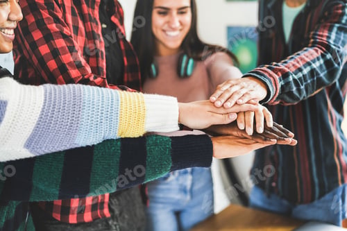 Preview: Multiracial young group of friends celebrating together stacking hands inside library room
