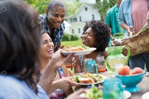 Preview: A group of adults and young people at a meal in a garden passing plates.