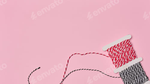 Preview: Two spools of red and white and black and white striped twine on a pink background.