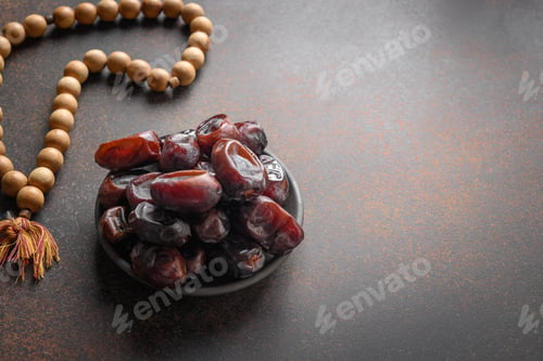 Preview: Ramadan. Wooden prayer beads and dates in bowl on brown. Eid Mubarak. Religious tradition.