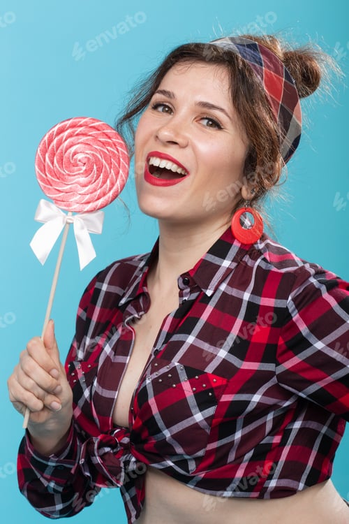 Preview: Charming young woman in retro clothes holding colorful lollipops in her hands and licking one posing