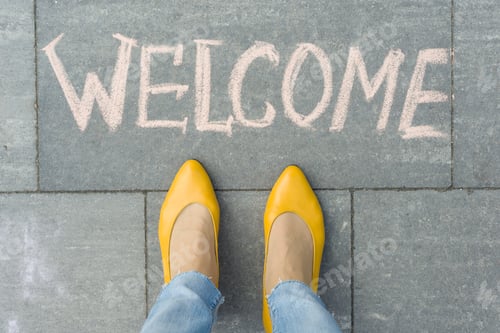 Preview: Female feet with text welcome written on grey sidewalk