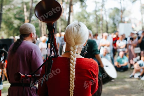 Preview: Back view of a woman musician in a medieval costume playing the bagpipes at an outdoor folk concert