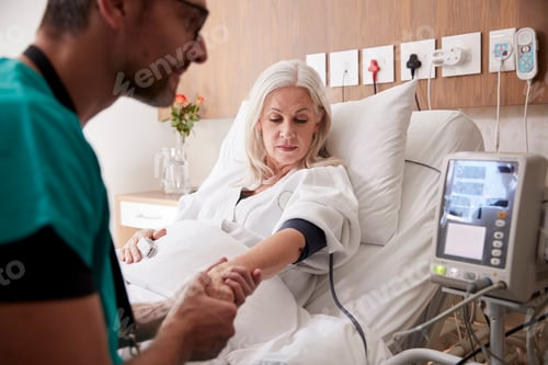 Preview: Male Nurse Taking Mature Female Patients Blood Pressure In Hospital Bed With Automated Machine