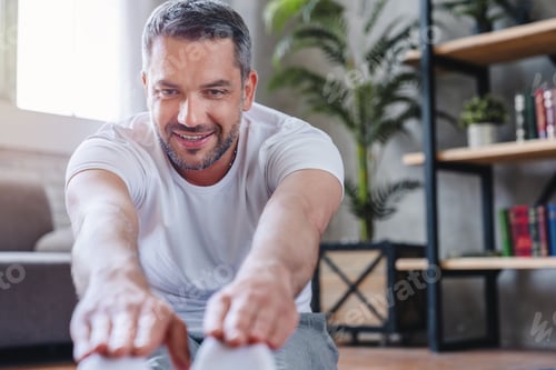 Preview: Close up of handsome adult sporty man stretching his legs at home
