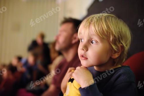 Preview: Cute little boy with his father watching cartoon movie in the cinema or performance in viewer hall