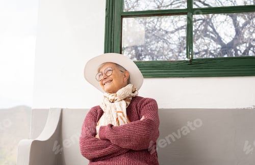 Preview: smiling senior gray haired woman sitting with crossed arms in outdoors looking away
