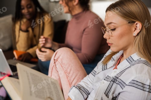 Preview: Diverse group female students learning at home using laptop and books for research.