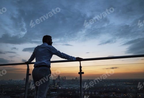 Preview: A rear view of businessman standing against London view panorama at dusk.
