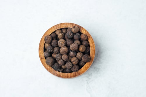 Preview: Explore allspice in wooden bowl on light background with focus on texture