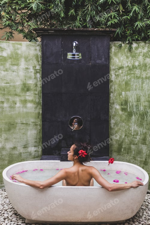 Preview: Woman relaxing in round outdoor bath with tropical flowers, organic skin care, luxury spa hotel