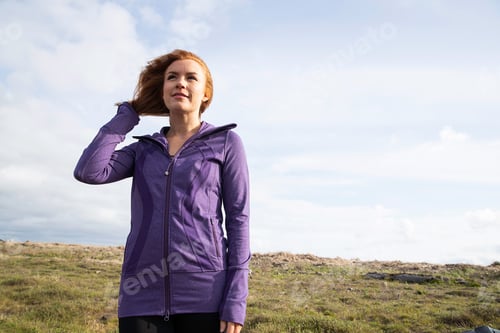 Preview: Redhead woman outside in countryside wearing purple workout jacket