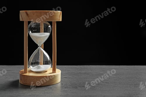 Preview: Hourglass with flowing sand on table against black background. Time management